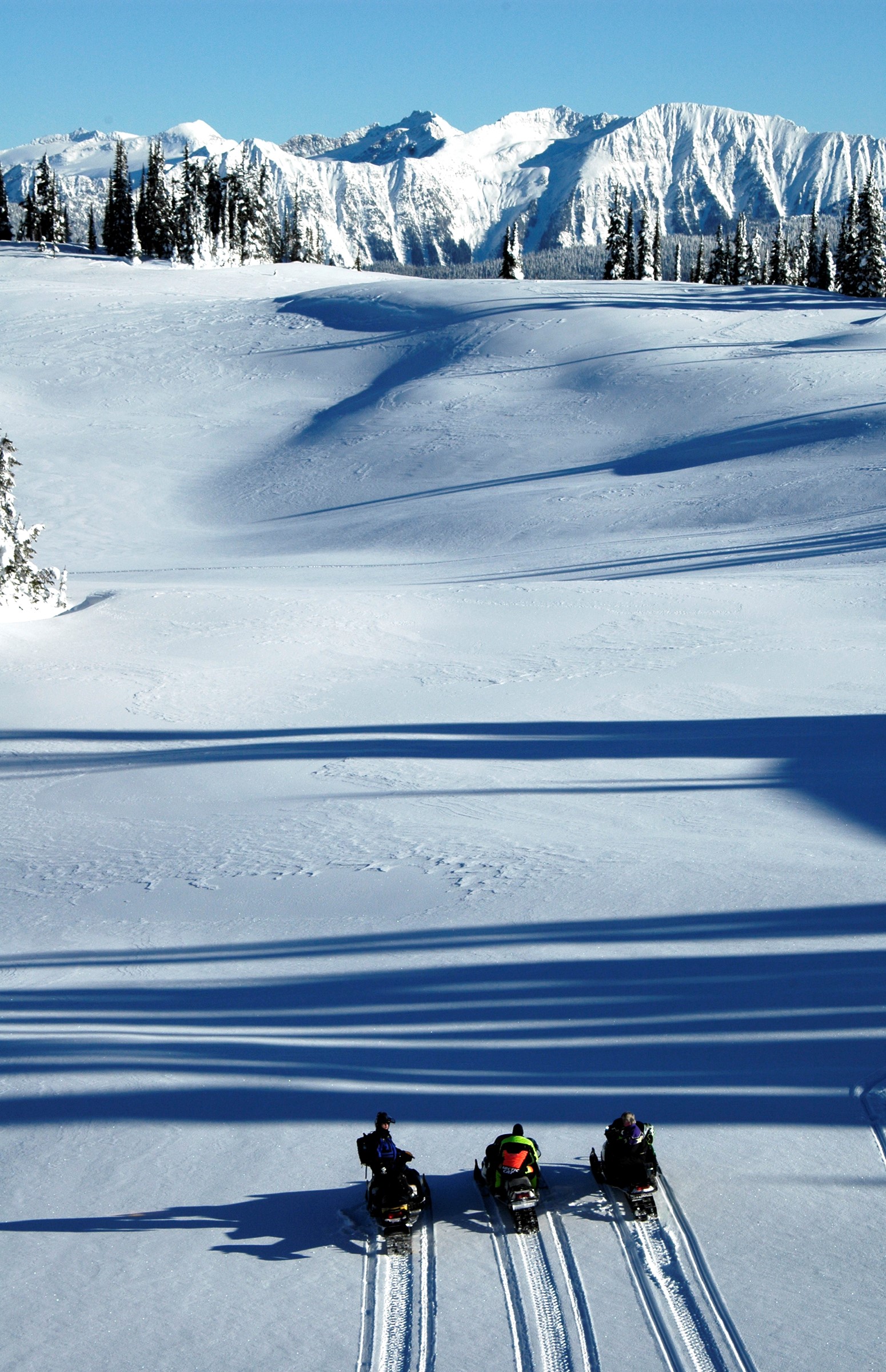 Three snowmobilers stopped in snowy mountain bowl