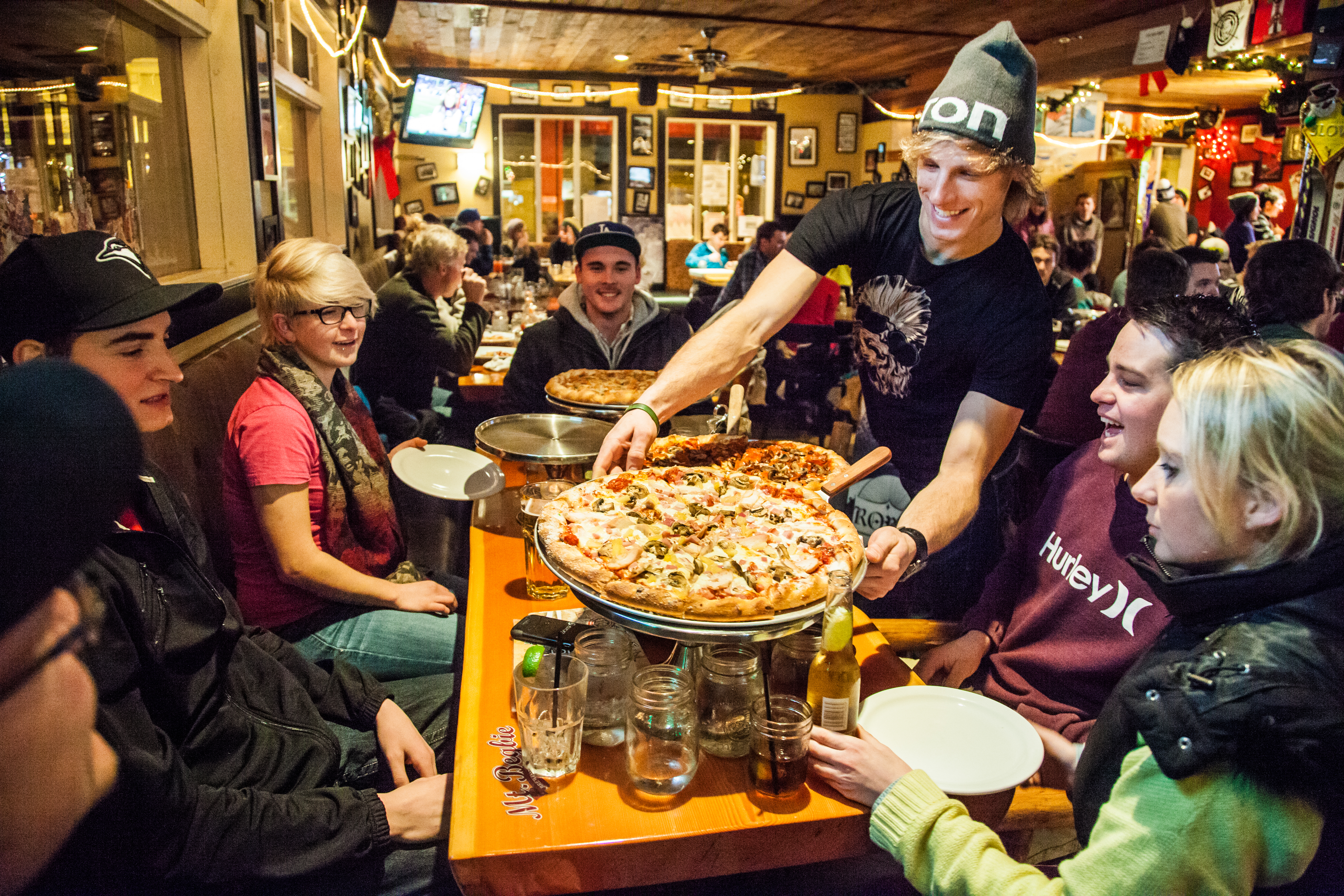 Server putting down a large pizza in front of a table of sledders